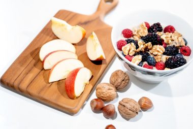 A vibrant breakfast bowl with mixed berries, walnuts, and apple slices on a rustic board.